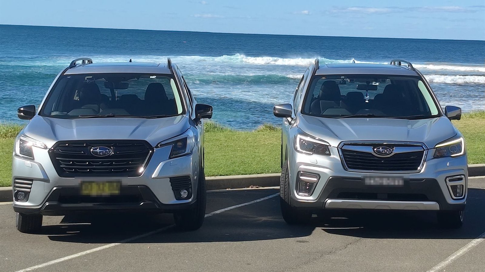 Both GP Drive cars parked side by side facing the ocean, a wave breaking behind them — the 2025 Subaru Forester STI on the left, the 2021 Forester on the right, both in silver.